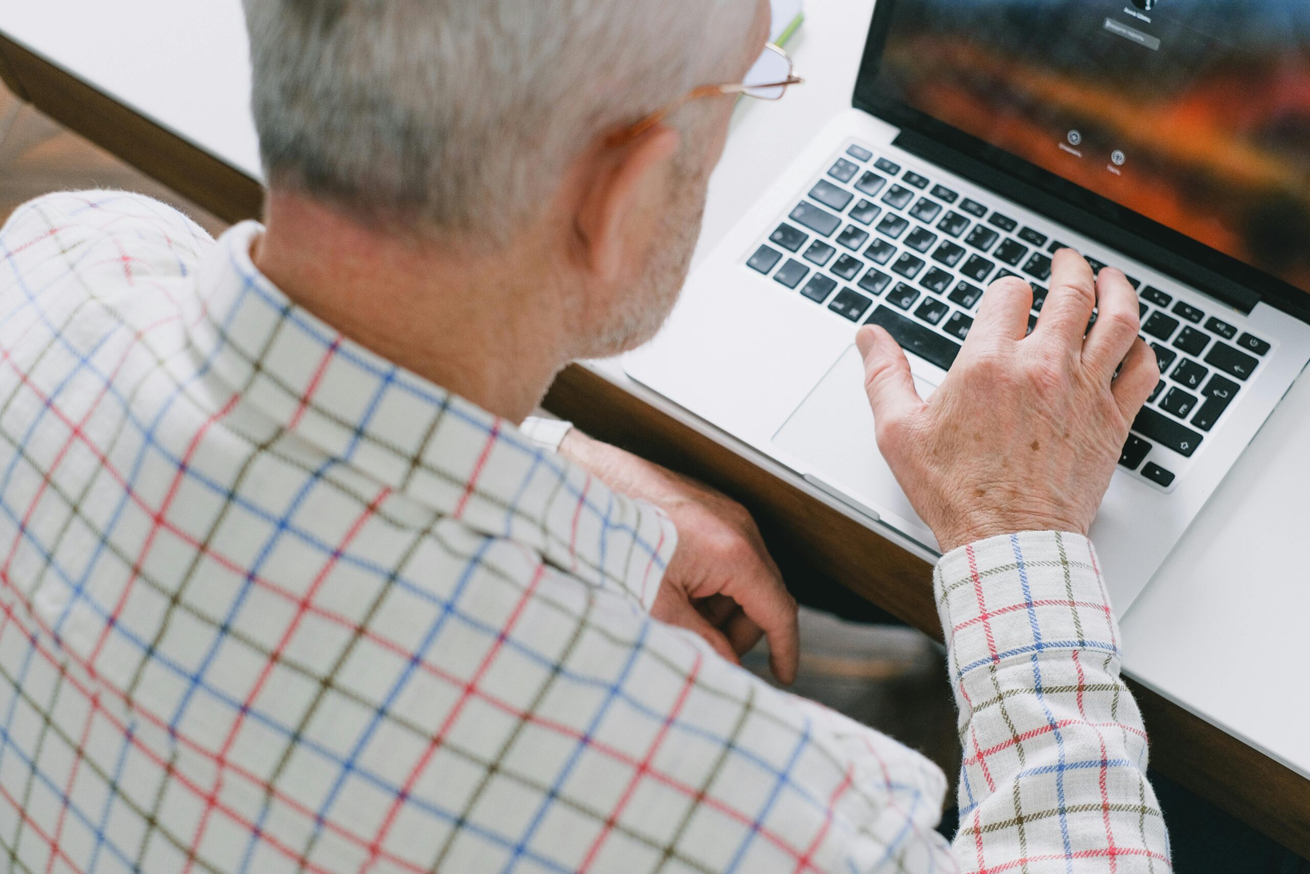 A senior adult in a plaid shirt using a laptop, showcasing digital engagement.